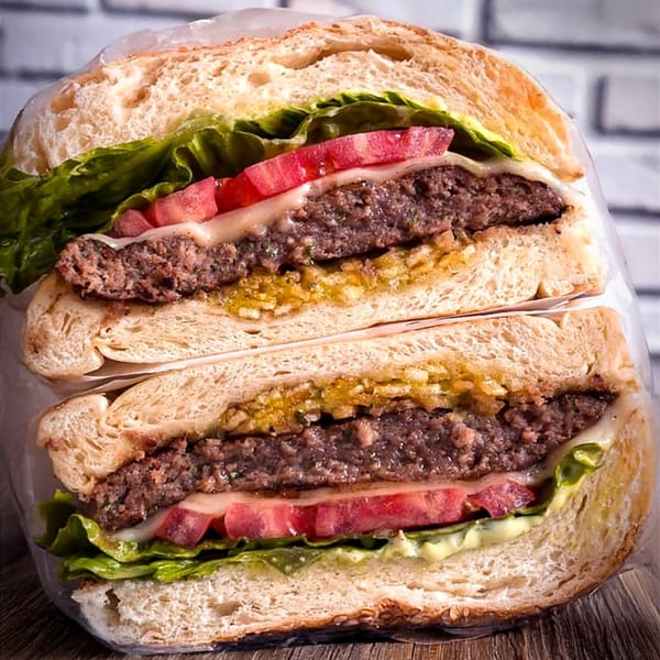 Cross-section of a Brazilian burger with two patties, cheese, lettuce, tomatoes, and sauce.