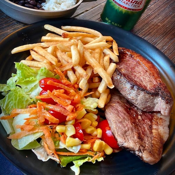 Brazilian steak with fries and a fresh salad, served on a black plate.