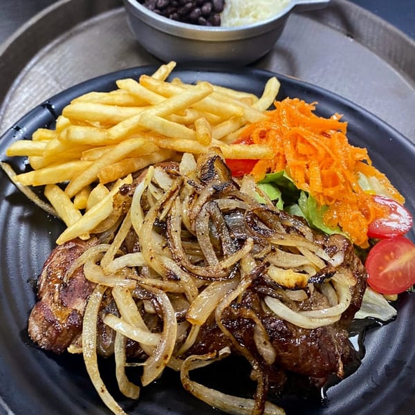Brazilian steak with caramelized onions, french fries, and a side salad with shredded carrots and tomatoes.