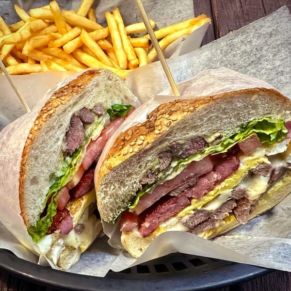 A Brazilian steak sandwich, cut in half, with lettuce, tomato, egg, and fries in the background.