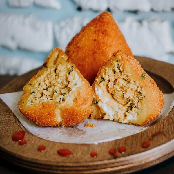 Three golden-fried coxinha, one whole and two cut open, revealing a savory chicken and herb filling.