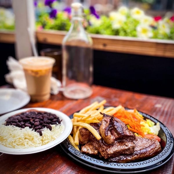Brazilian steak with fries and salad, alongside rice and black beans, on a wooden table.