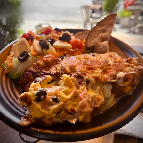 A Brazilian breakfast plate with scrambled eggs, salad, and toast on a dark plate.